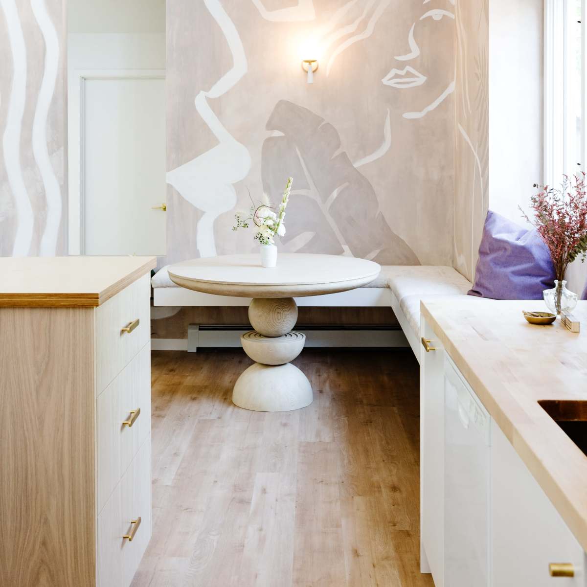 A modern kitchen features a round table in front of a wall adorned with abstract mural art and natural light coming through the windows.