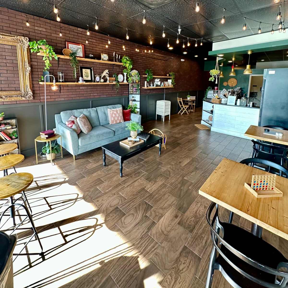 A cozy café interior with a gray sofa, wooden tables, and string lights hanging from the ceiling.