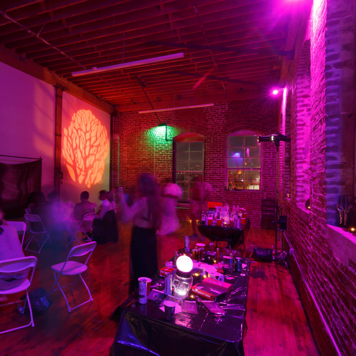 A dimly lit event space features people sitting at tables, with colorful lighting and a decorative projection on the wall.