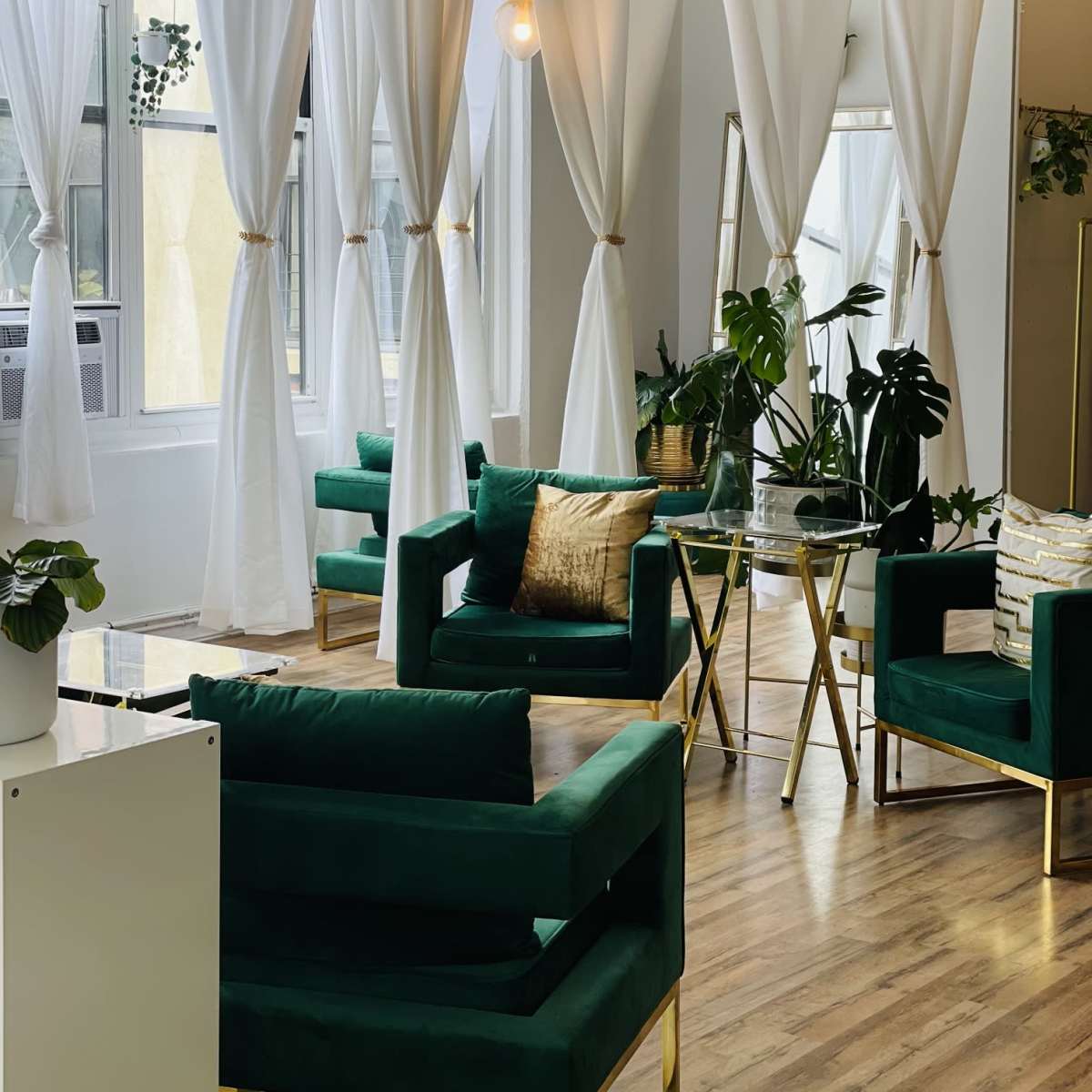The interior features a bright room with large windows, green upholstered chairs, hanging light fixtures, and white curtains creating a cozy atmosphere.