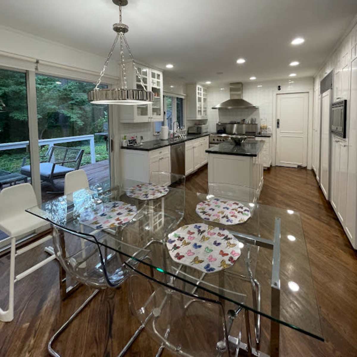 A modern kitchen with a glass dining table and a view of a deck surrounded by trees.