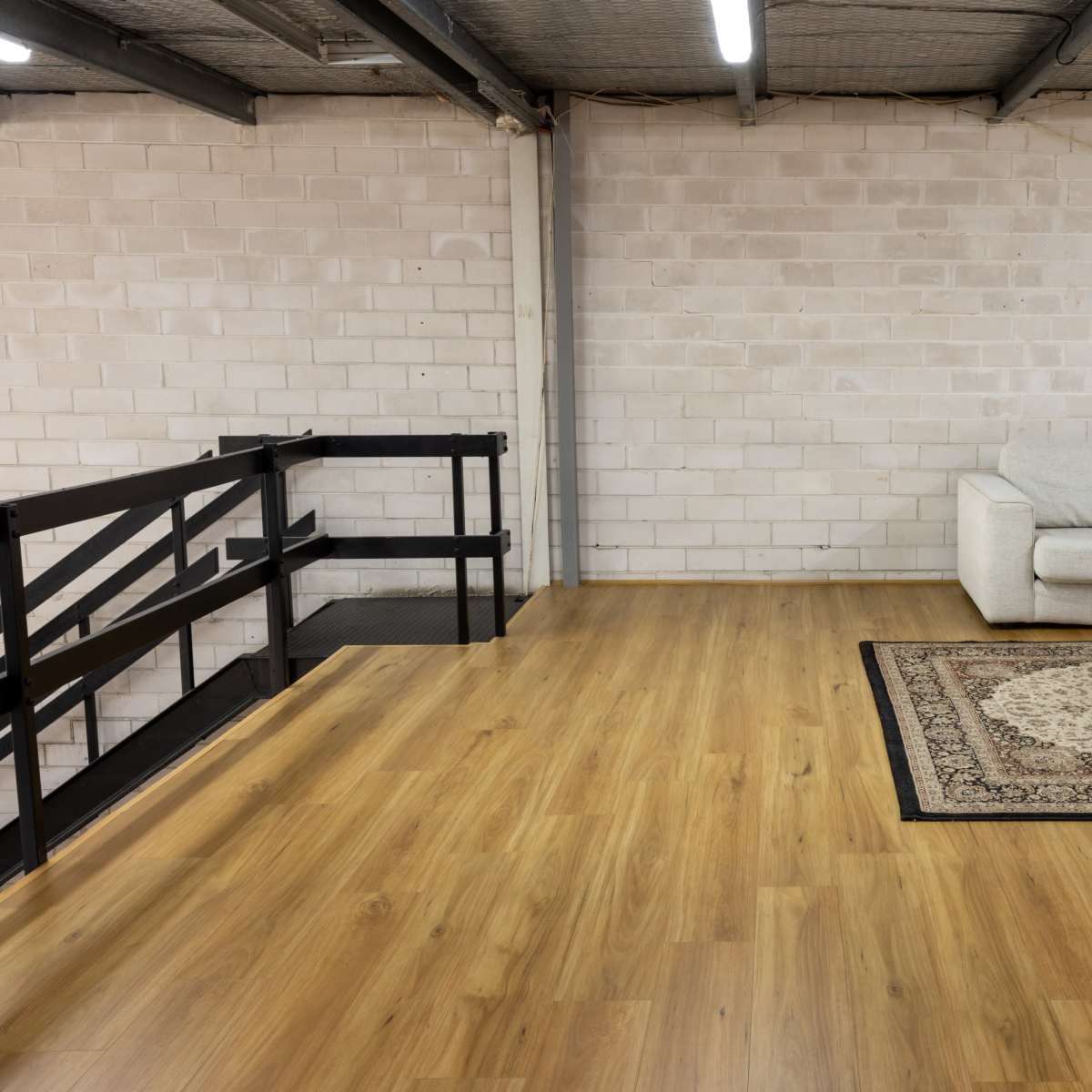 A spacious, minimally furnished room with a couch, a coffee table on a patterned rug, and a railing leading to a lower level.
