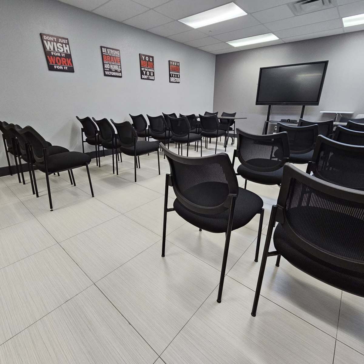 A conference room with several black chairs arranged in rows, a large screen at the front, and motivational posters on the walls.