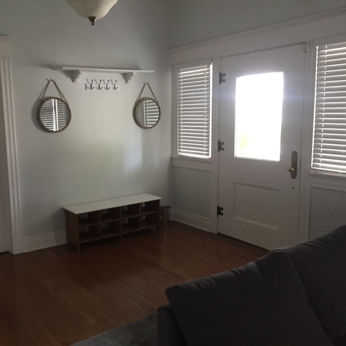 The room features a wooden floor with a bench, two mirrors above it, and a door with window panes beside it.