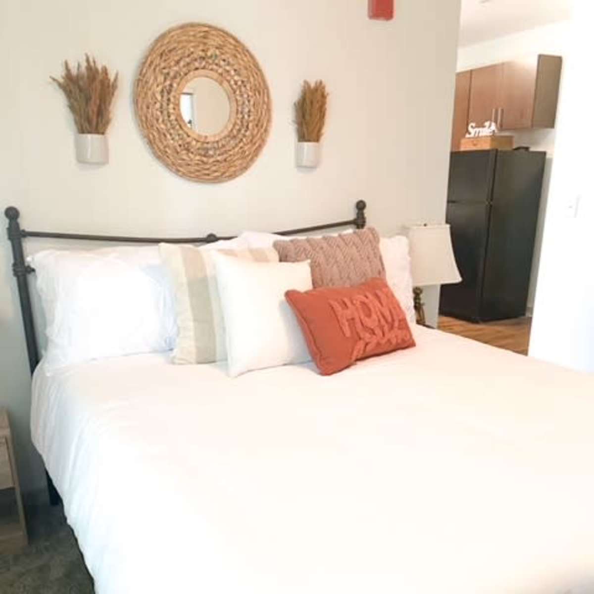 A neatly made bed with decorative pillows, a round mirror above it, and a nightstand beside the bed in a well-lit room.