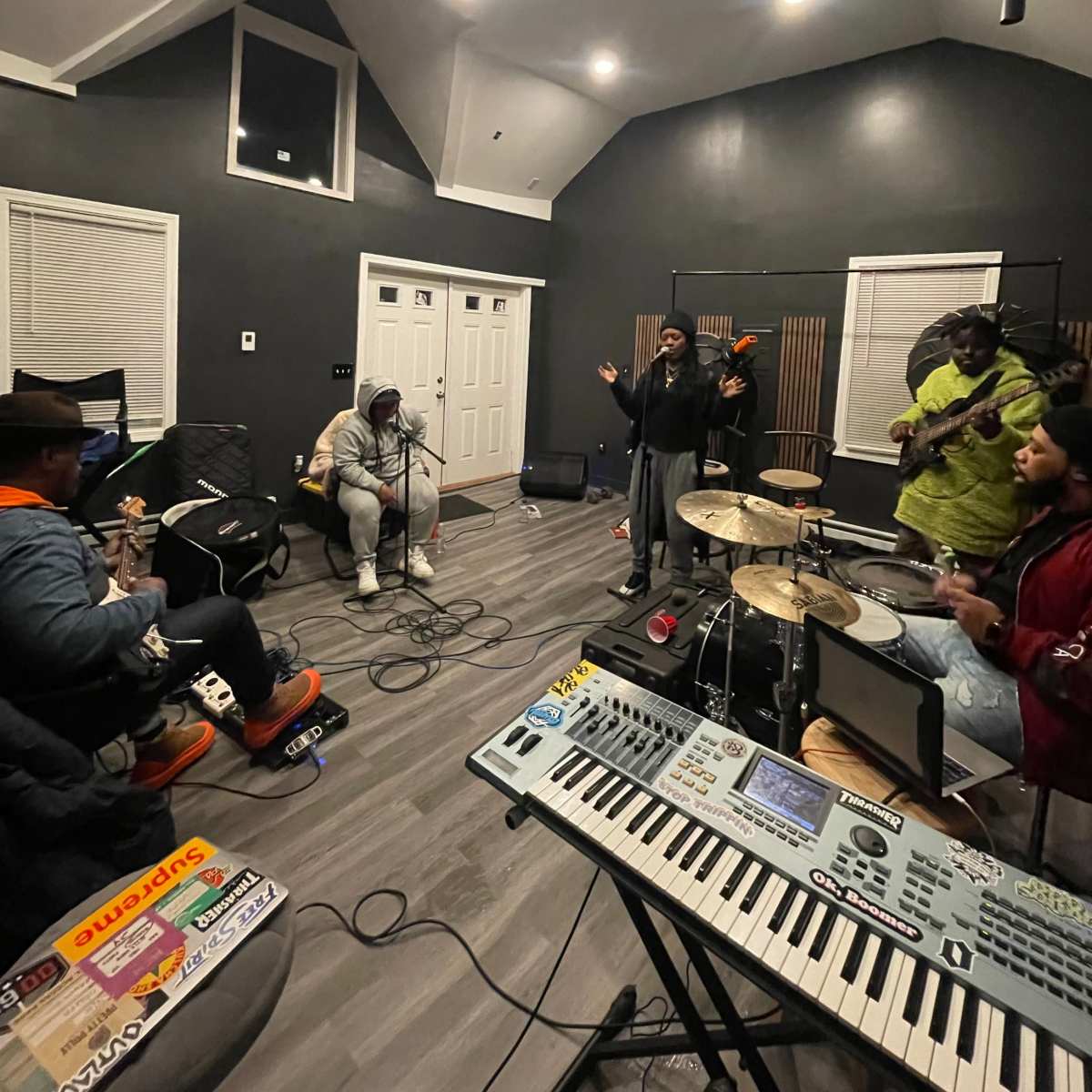 A group of musicians plays instruments and sings in a spacious recording studio with modern lighting and sound equipment.
