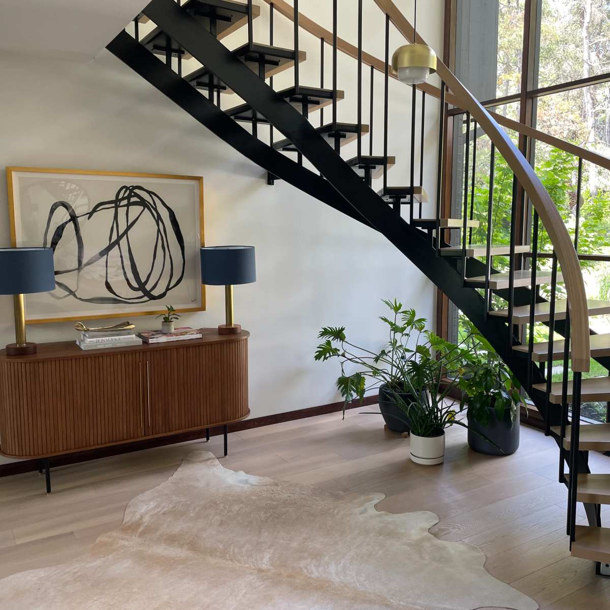 A spiral staircase leads from a modern entryway to a bright space filled with plants and natural light.