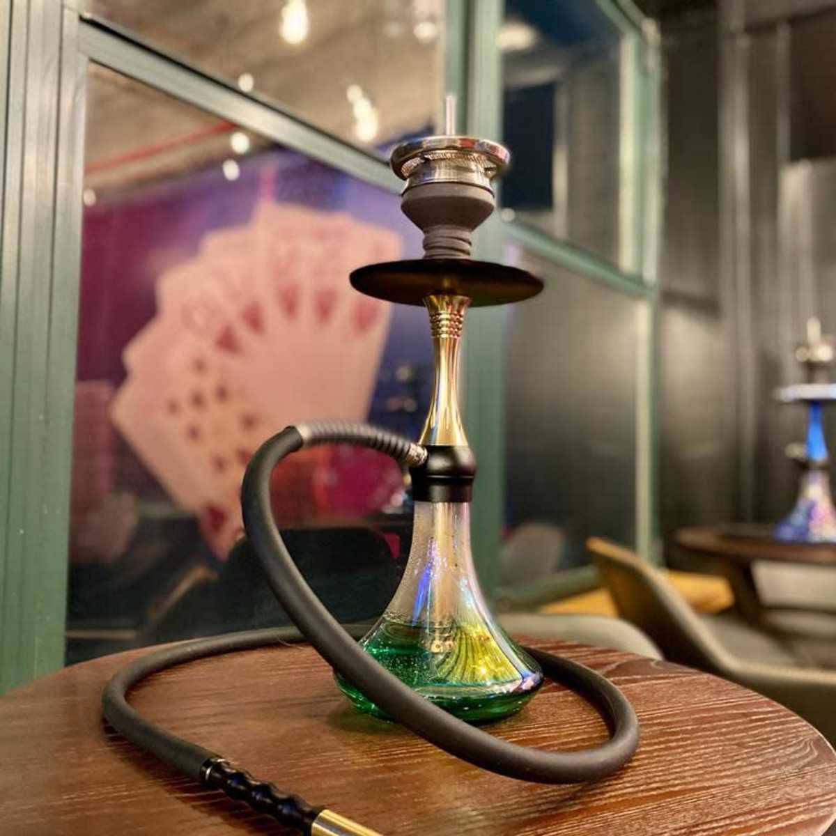 A hookah with a colorful base sits on a wooden table, with playing cards displayed in the background.