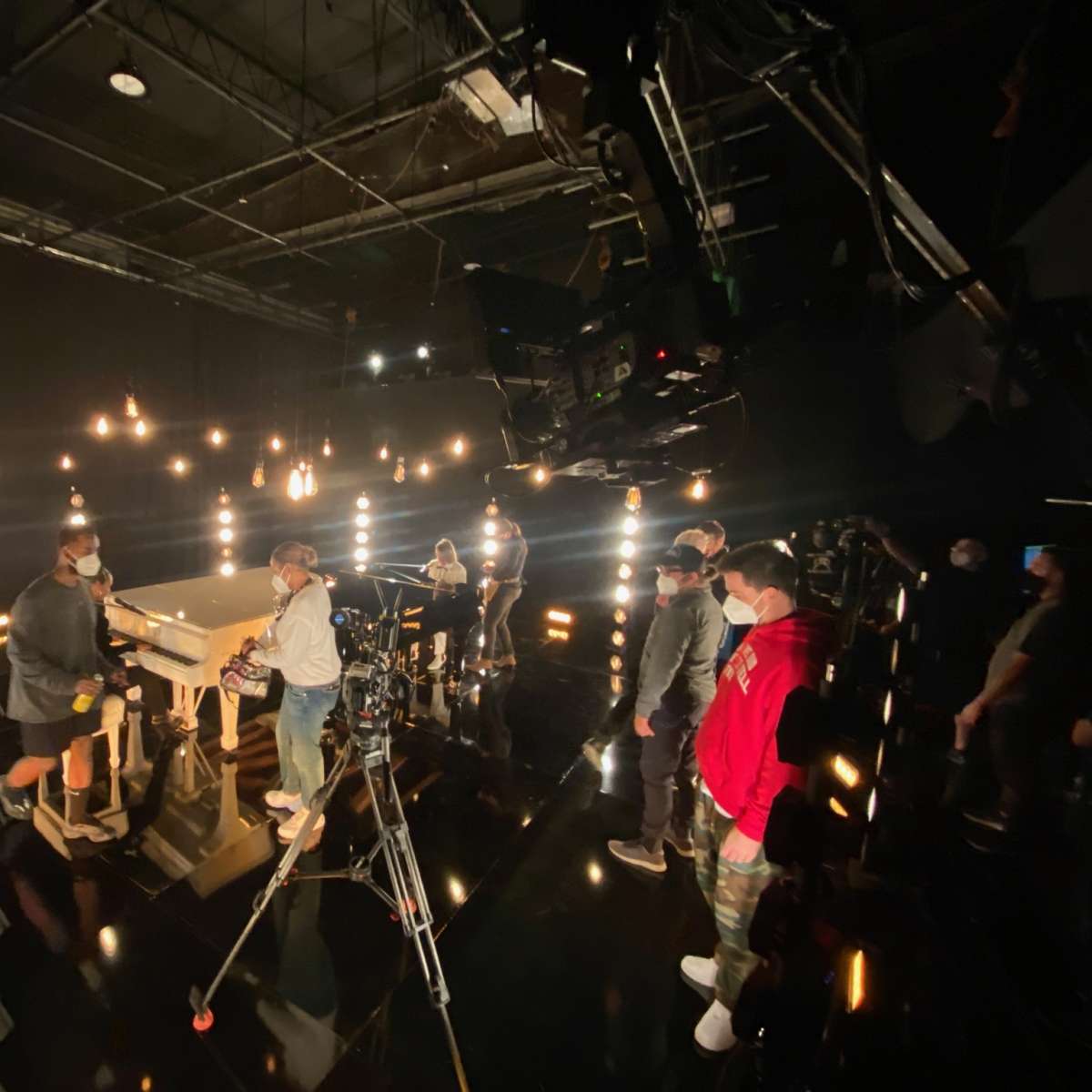 A film crew works around a central table in a dimly lit studio, with lights suspended above and cameras positioned for a shoot.