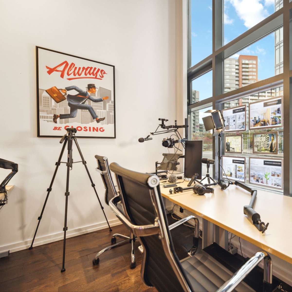 A modern office space with a large window, a desk equipped with multiple monitors, and various tripods and desk lamps.