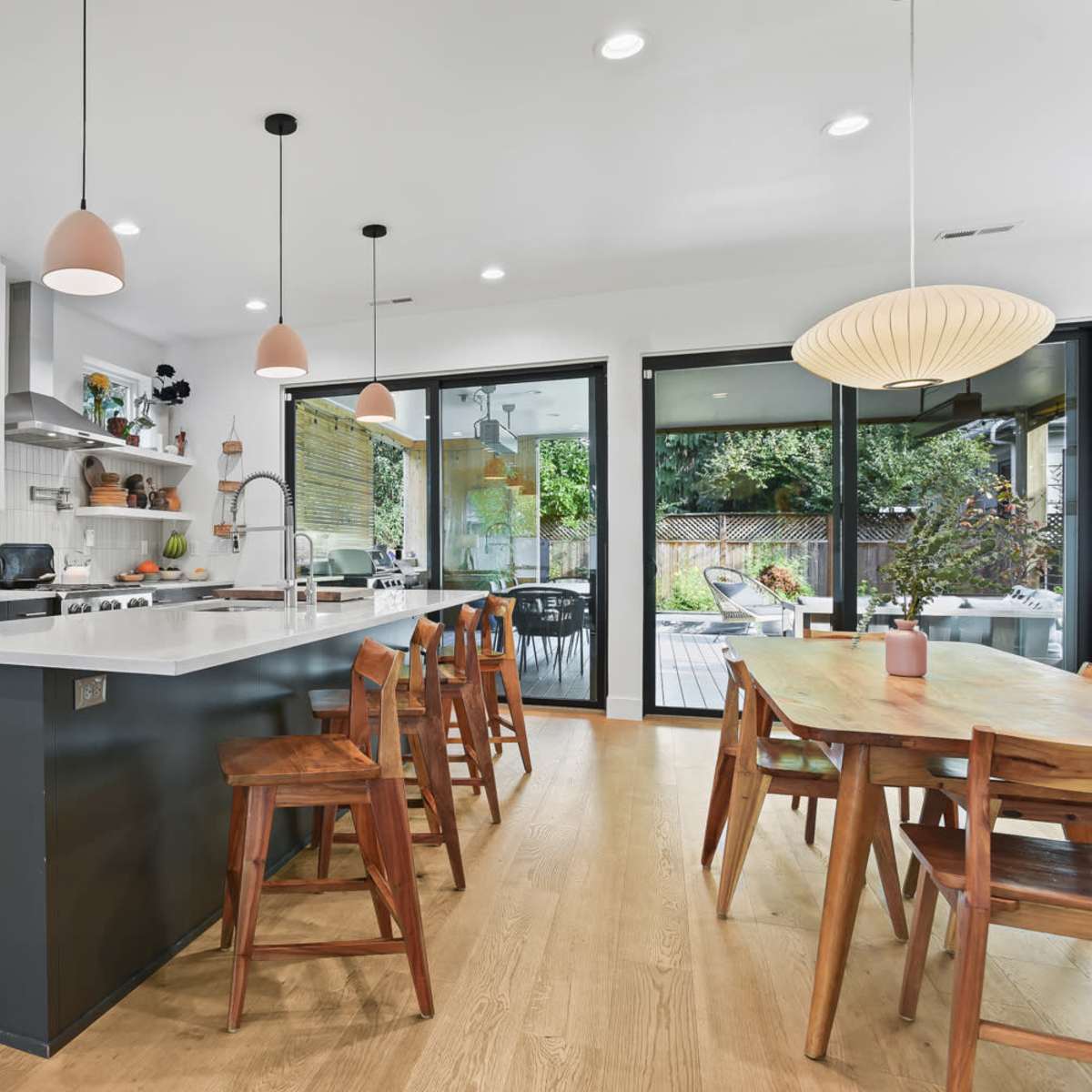 A modern kitchen features a large island with bar stools, sleek appliances, and ample natural light from windows facing a patio.