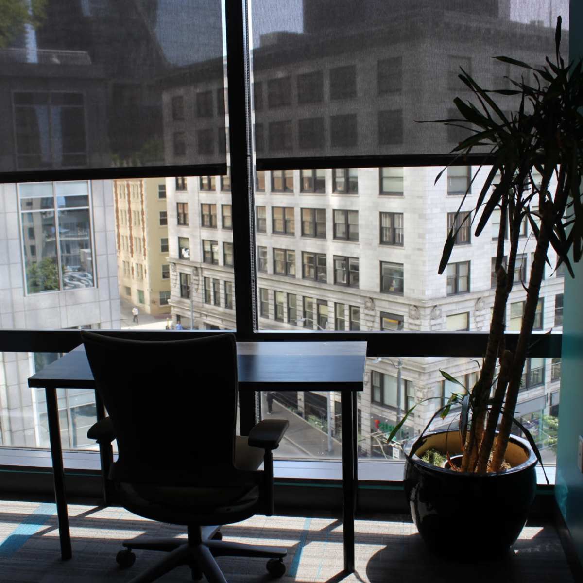 A desk and chair are positioned next to a large window with a view of a city street and nearby buildings.
