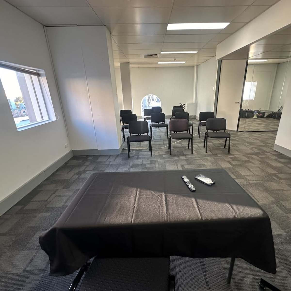 A conference room features a black table at the center, with a notepad and pen, surrounded by several chairs arranged in rows against the wall.