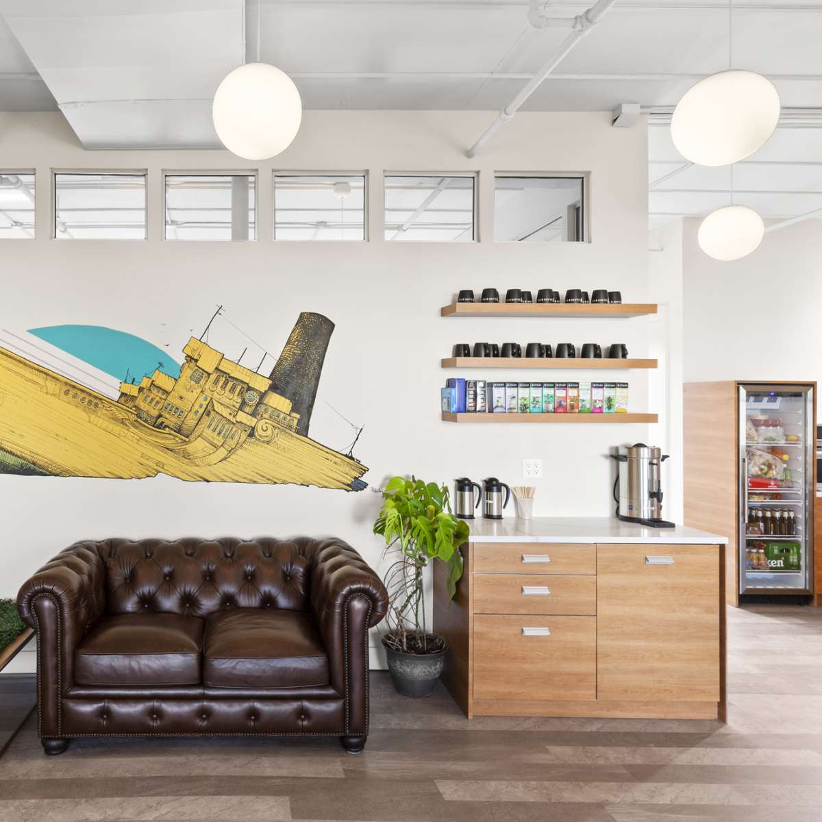 A modern interior with a brown leather sofa next to a wall featuring a large mural of a yellow ship, along with shelving that holds various containers.