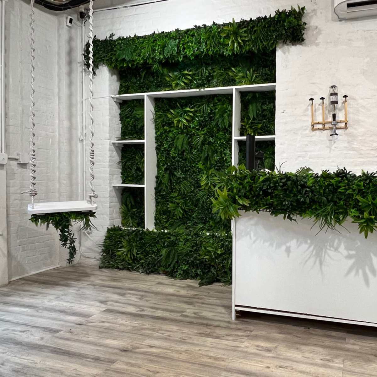 A clean, modern reception area featuring a white counter with greenery adorning its front and a wall covered in plants.