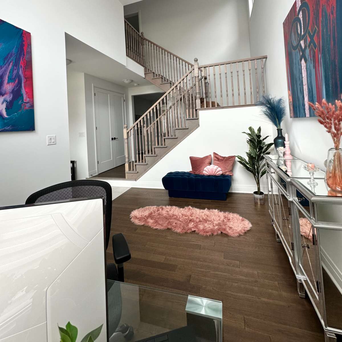 A bright, modern living space featuring a staircase, a blue couch, decorative plants, and colorful wall art.