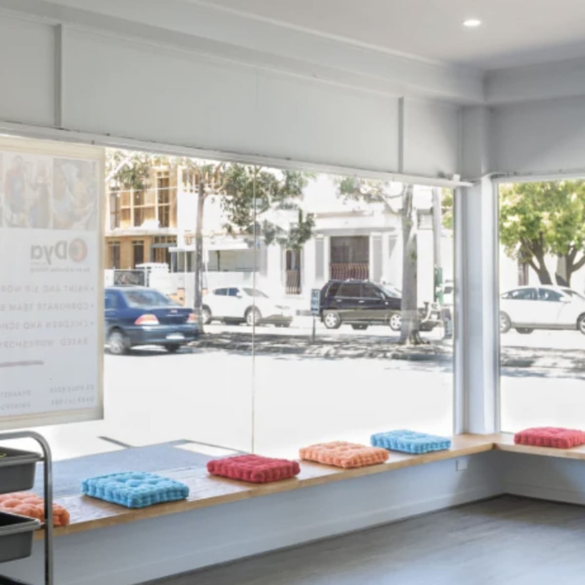 A bright, modern waiting area with large windows, benches lined with colorful cushions, and a cart in the corner.