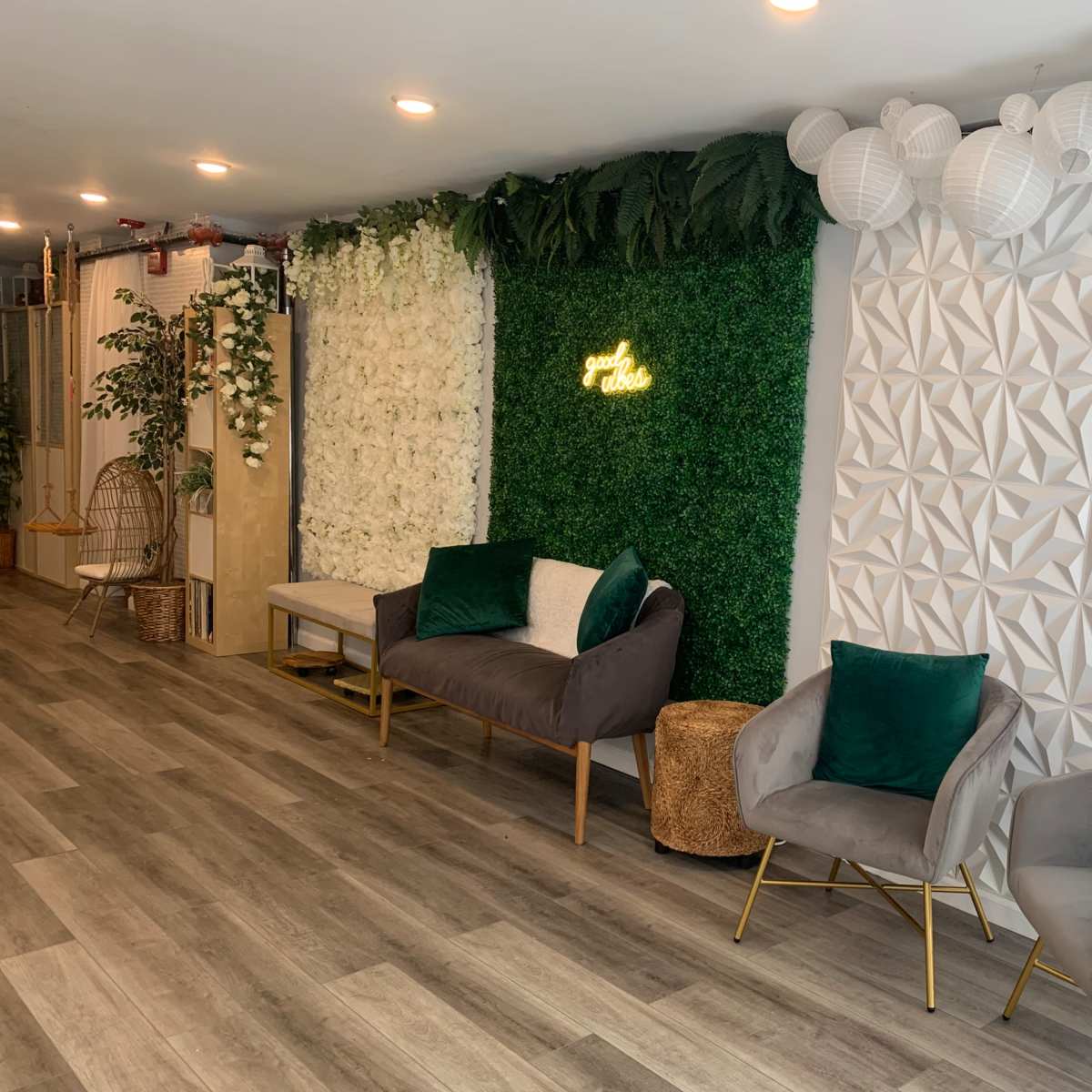 The scene features a modern lounge with green wall decor, two gray armchairs with green cushions, and a textured white wall illuminated by decorative hanging lights.