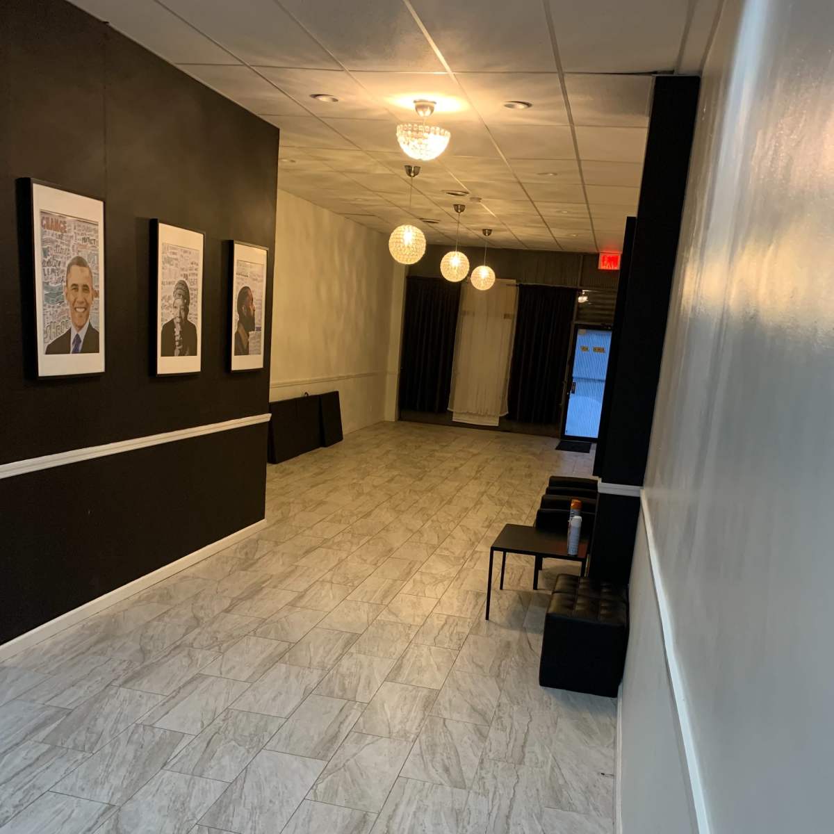 A long hallway with framed portraits on the left wall, a black curtain at the end, and a few light fixtures hanging from the ceiling.