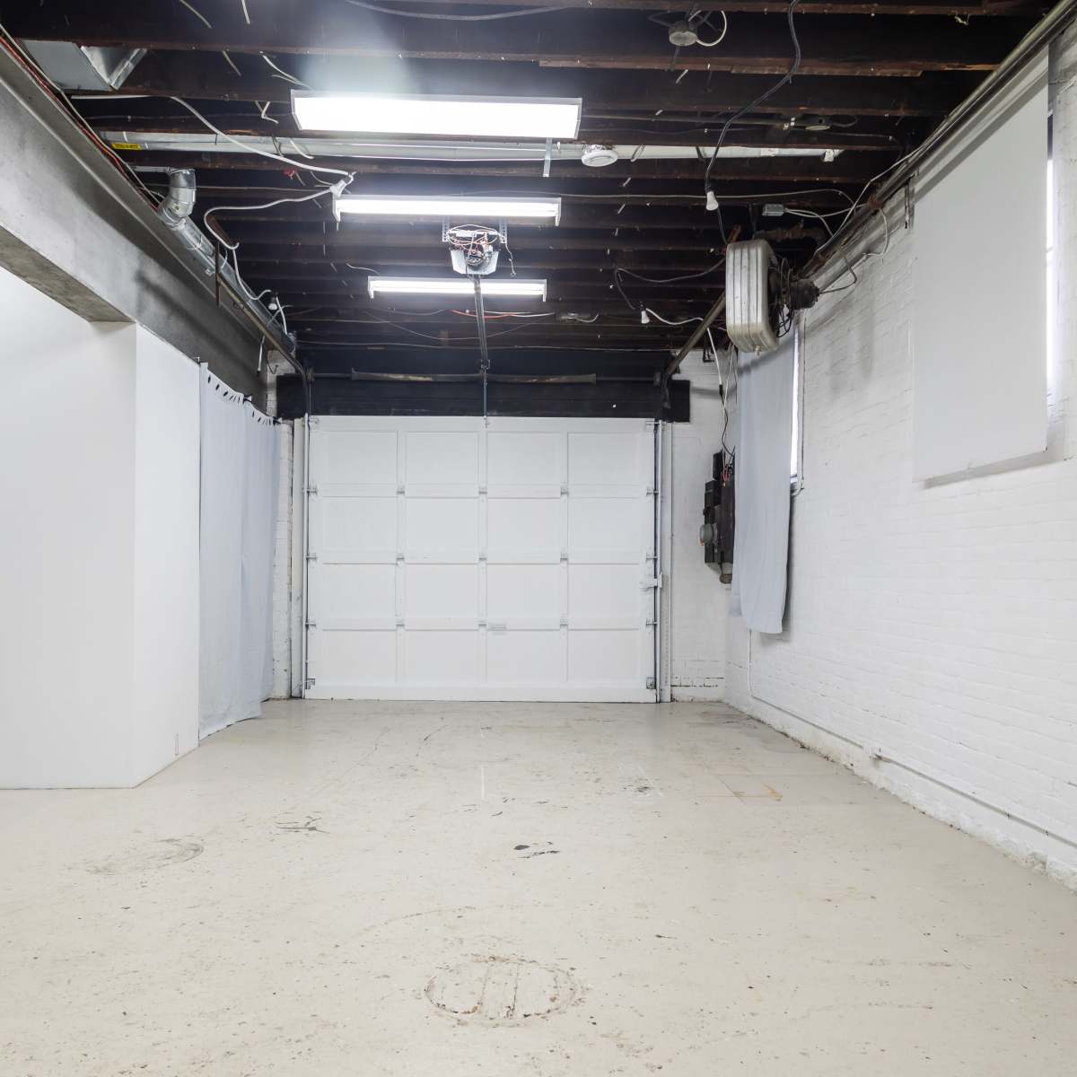 A vacant interior space with exposed beams and a large garage door at one end.