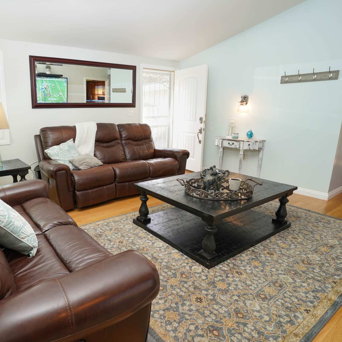 A living room with two brown leather sofas, a dark coffee table, and a rug, all illuminated by natural light coming through a window.