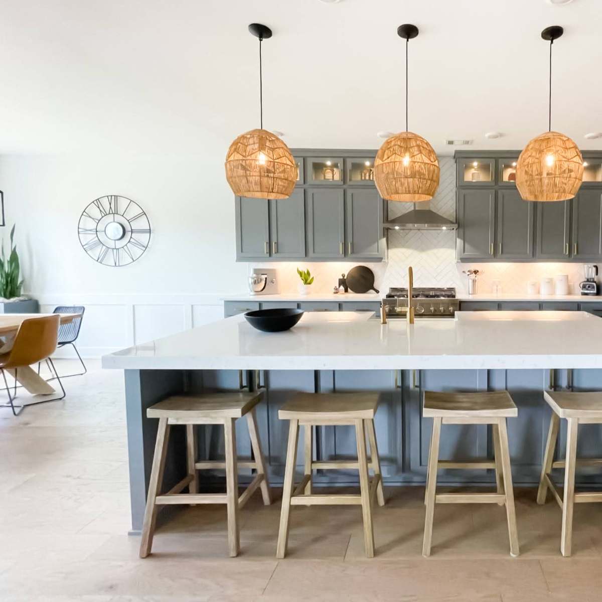 The kitchen features a large island with three pendant lights overhead, surrounded by wooden stools and modern cabinetry.