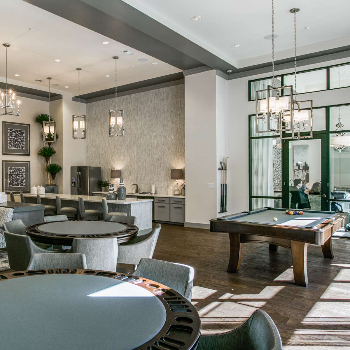 A modern lounge area featuring tables, chairs, and a pool table, with large windows allowing natural light to fill the space.