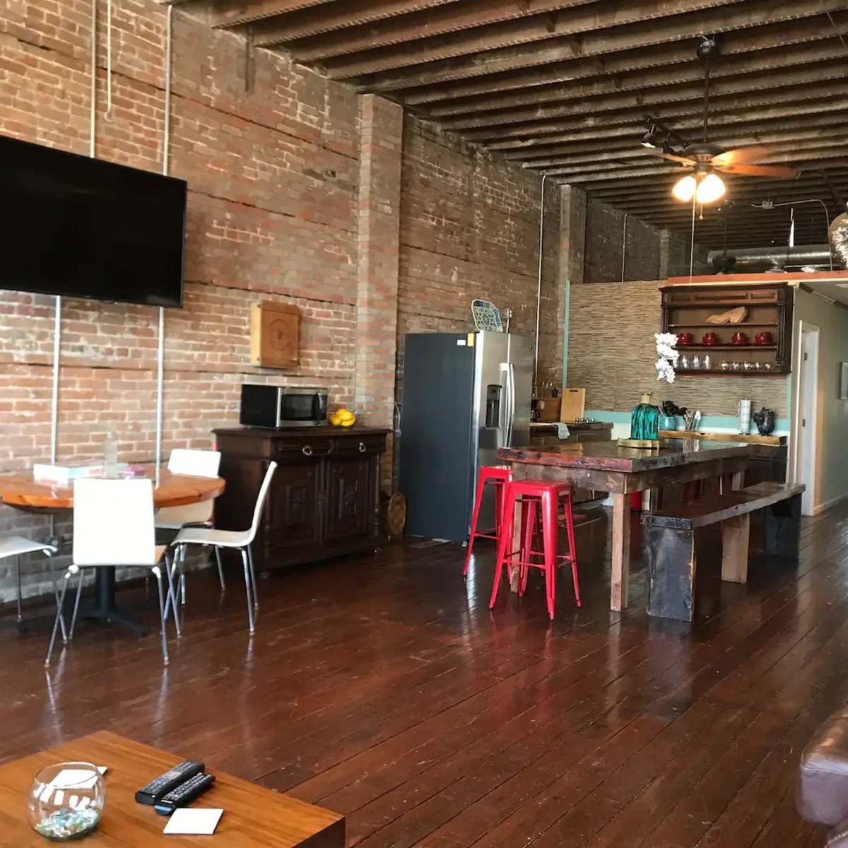A spacious kitchen and dining area features exposed brick walls, wooden floors, and a large island with red stools.