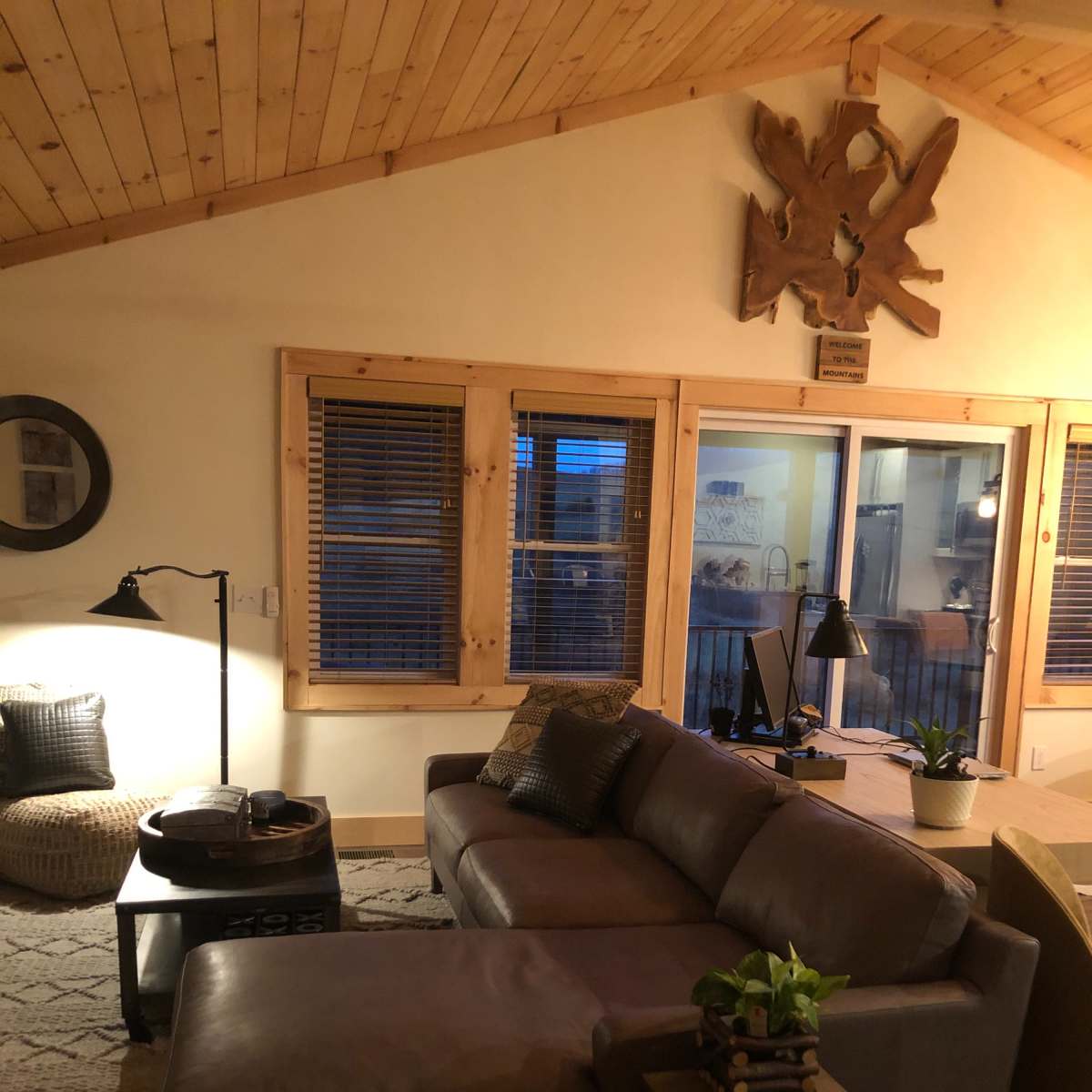 A cozy living room with a leather sectional sofa, a round coffee table, a floor lamp, and large windows that allow natural light to enter.