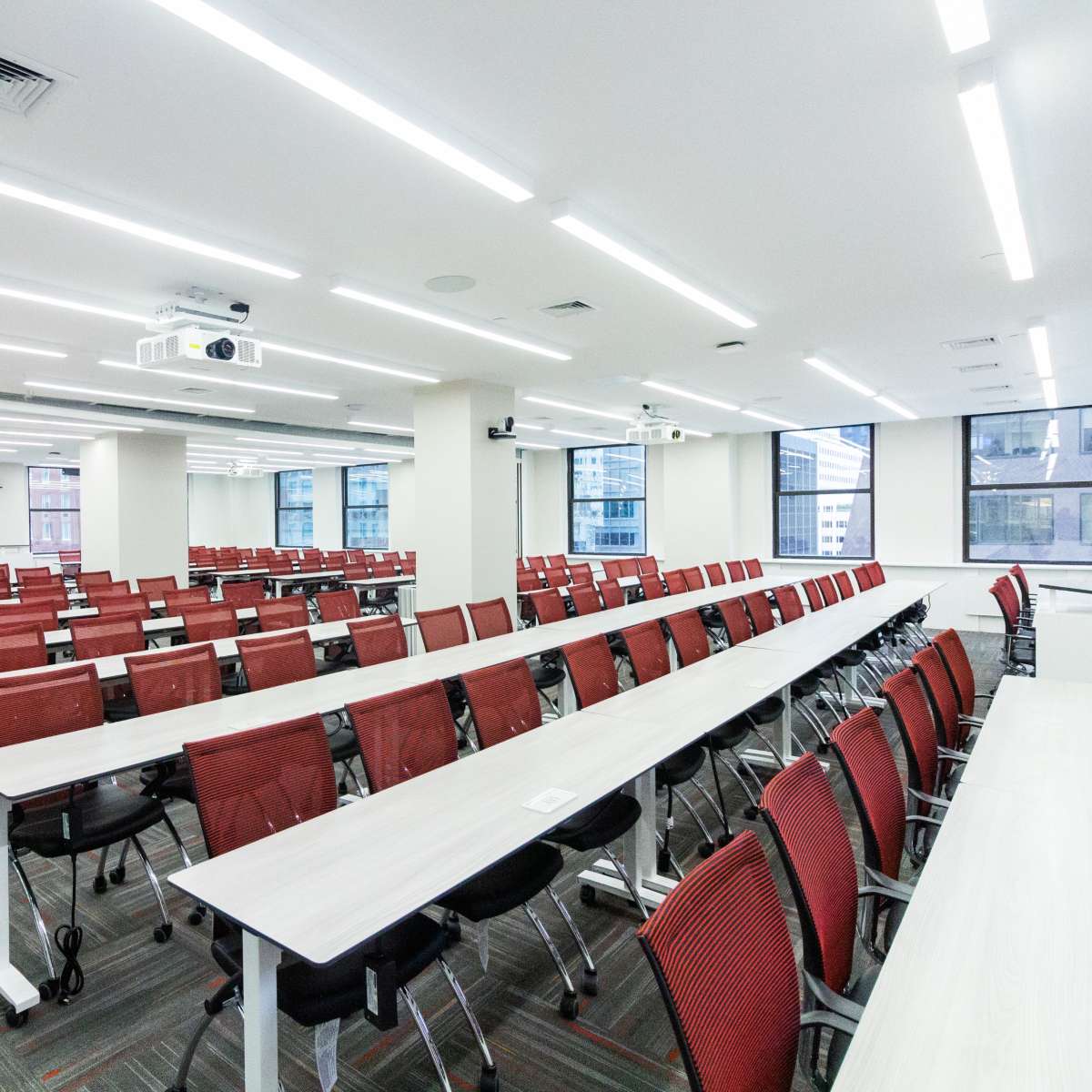 A modern, spacious classroom with rows of tables and red chairs arranged for a seminar or meeting.