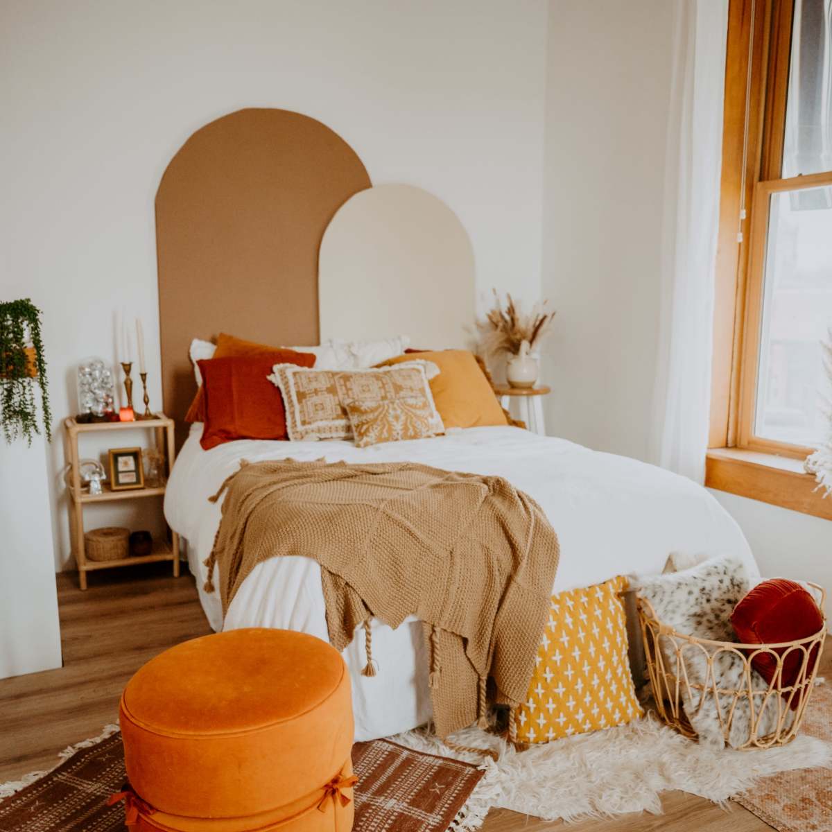 A cozy bedroom featuring a bed with decorative pillows and a throw, a soft rug, and a wooden chair beside a side table with various decorative items.