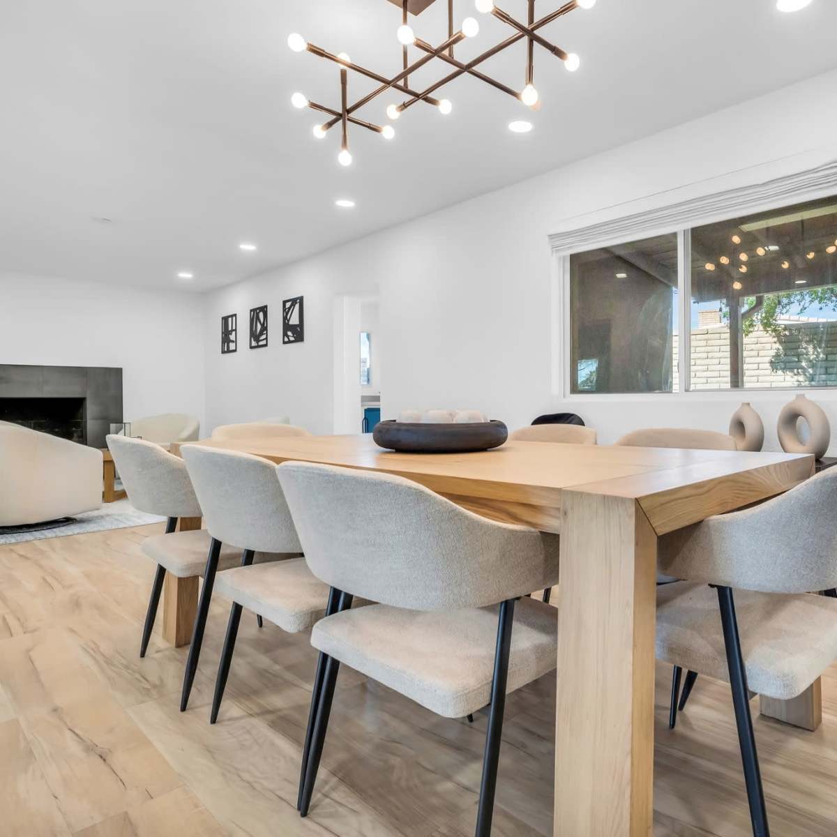 A light-filled dining area features a wooden table surrounded by upholstered chairs, with a window overlooking an outdoor space.