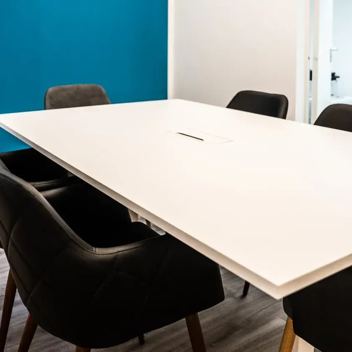 A modern conference room with a large white table surrounded by black chairs and a blue accent wall.