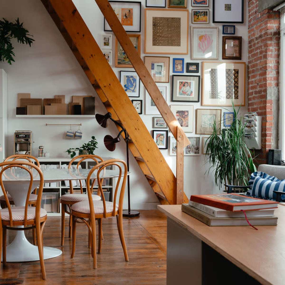 A dining area features a round table surrounded by wooden chairs, with a background of a gallery wall and exposed wooden beams.