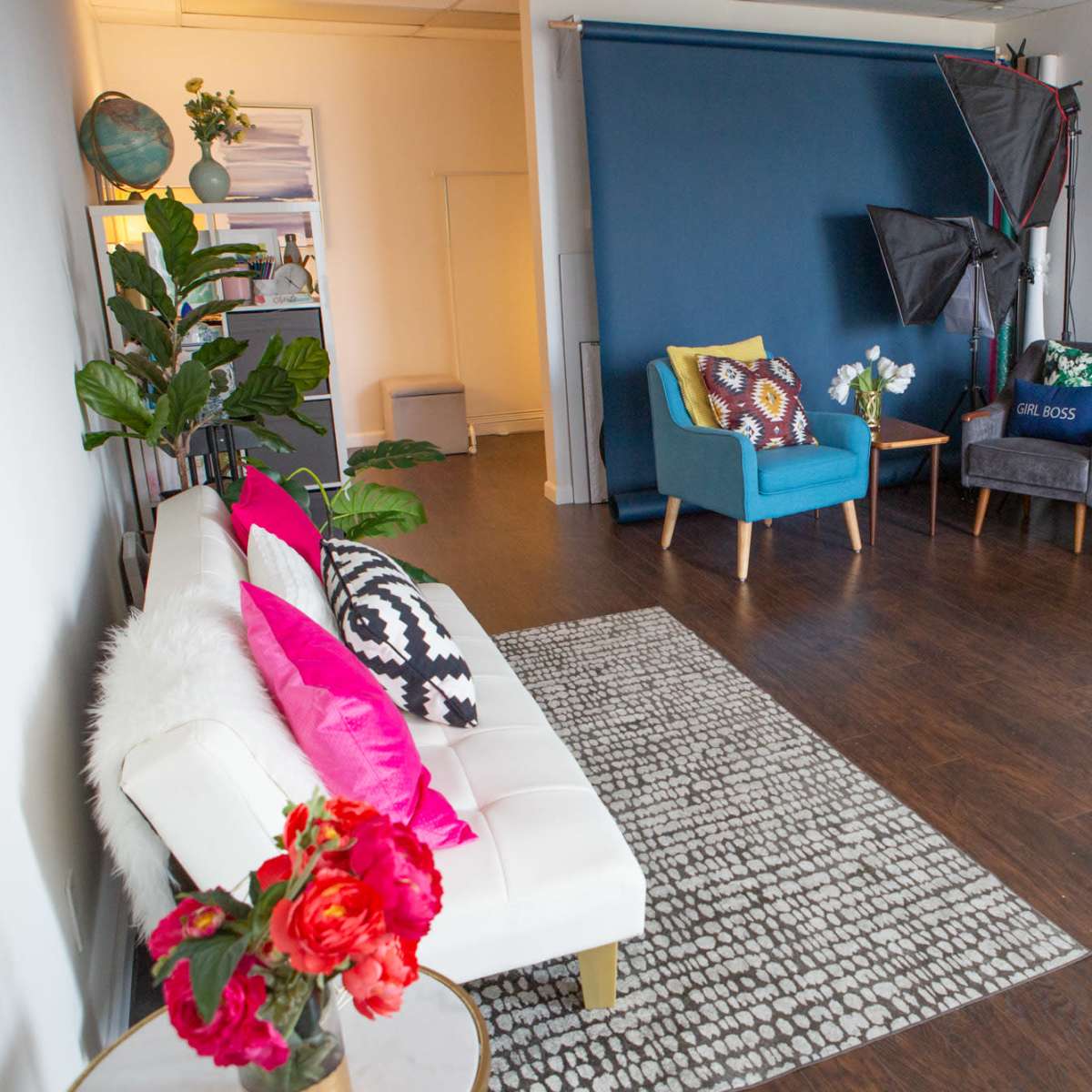A bright interior space featuring a white sofa, a gray couch, two accent chairs, a patterned rug, and a small round table with flowers.