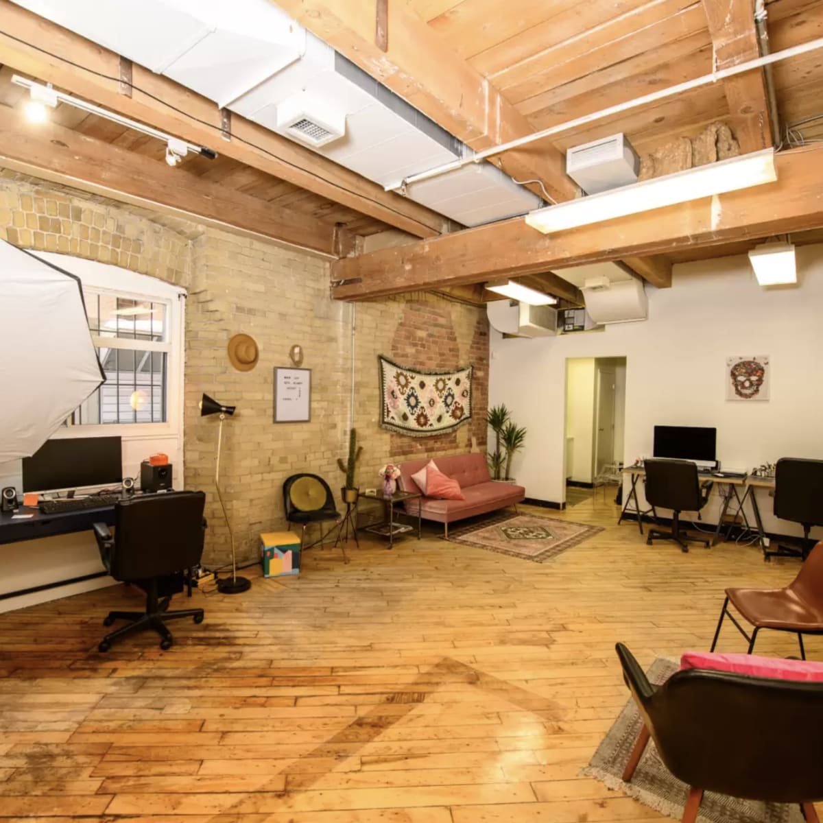A bright, open office space with wooden beams, a mix of workstations, and a seating area featuring a pink couch and decorative elements.
