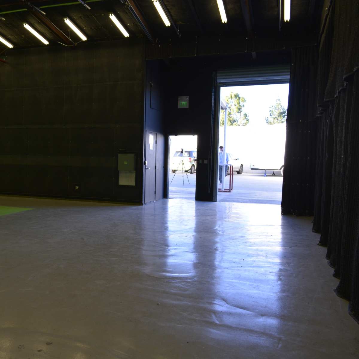 A spacious film studio with a green screen wall on one side and an open door leading outside on the opposite side.