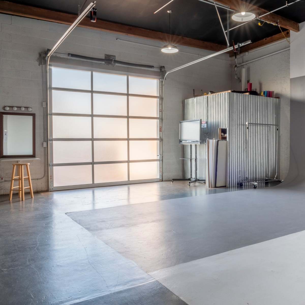 A spacious studio with a large garage door, a metal storage unit, a flat screen TV, and a bare, light gray backdrop.