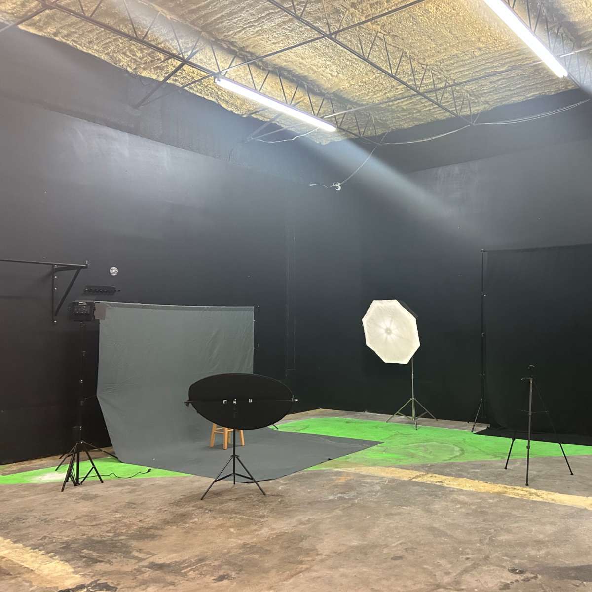 A photography studio with a black painted background, various lighting equipment, and backdrops arranged on the floor.