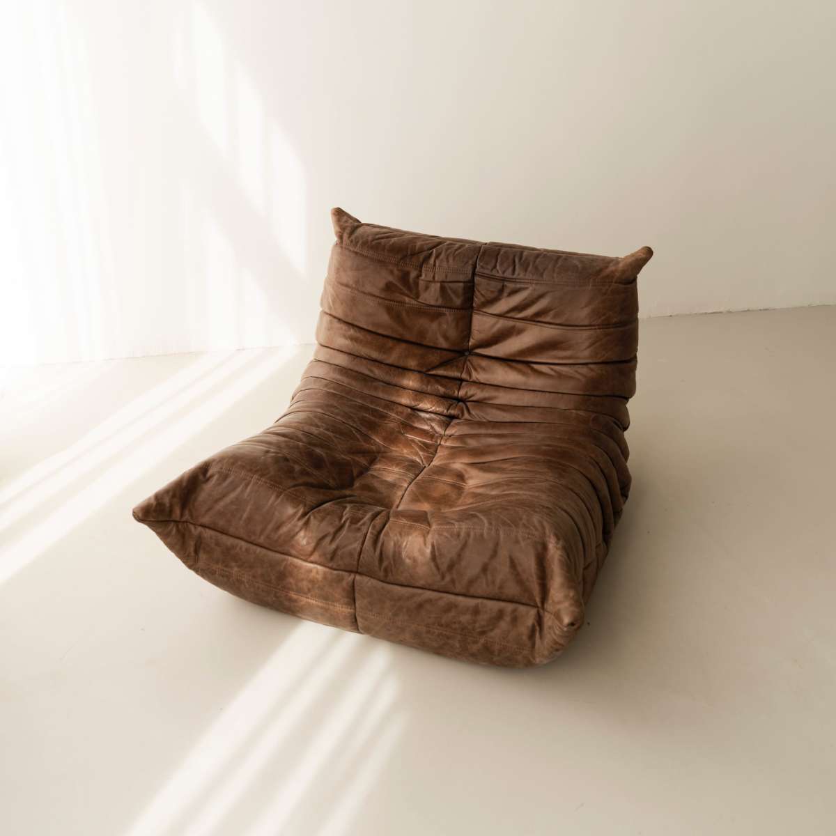 A brown, plush chair is positioned on a light-colored floor, illuminated by soft natural light streaming through a nearby window.