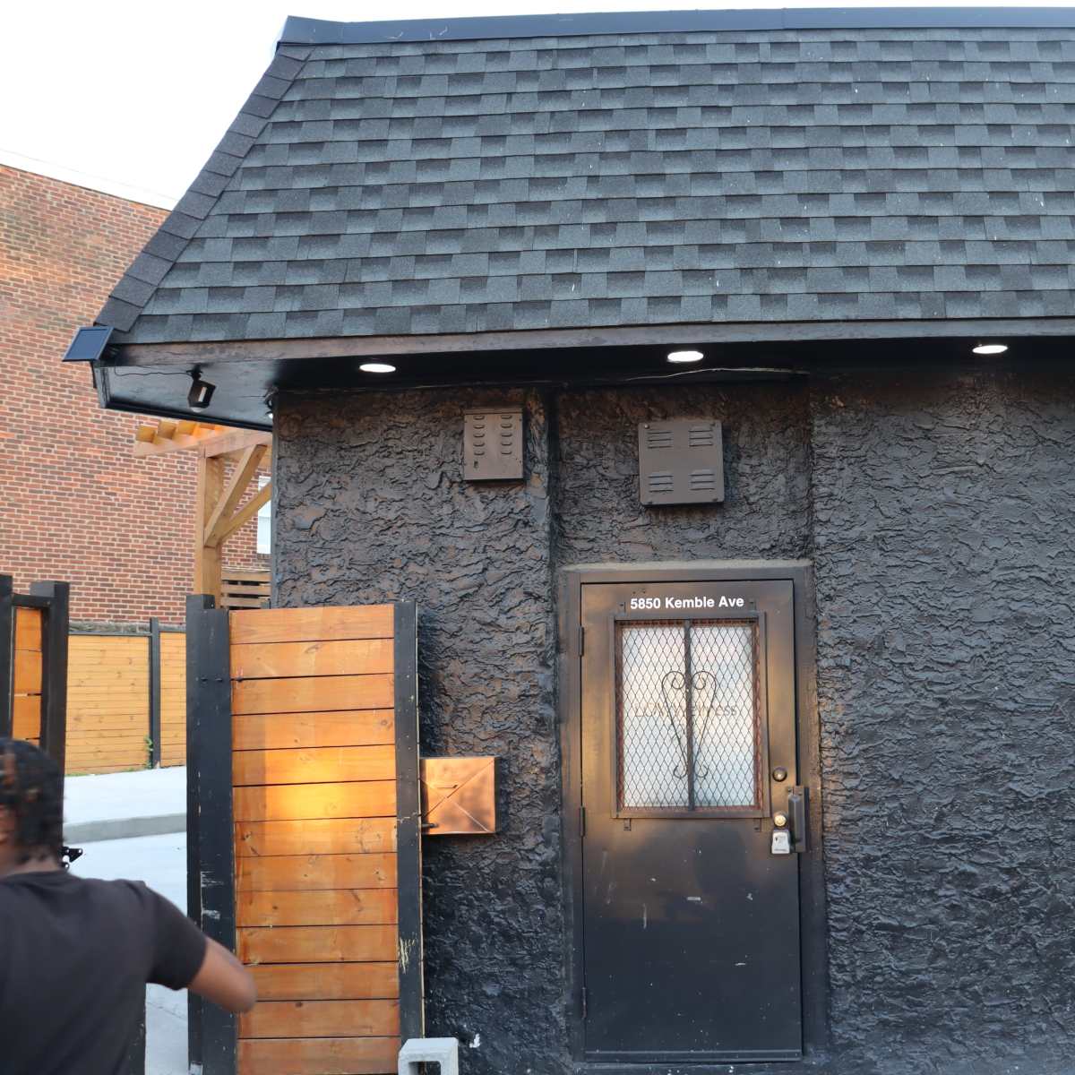 A black textured building with a sloped roof and a door featuring a metal grate.