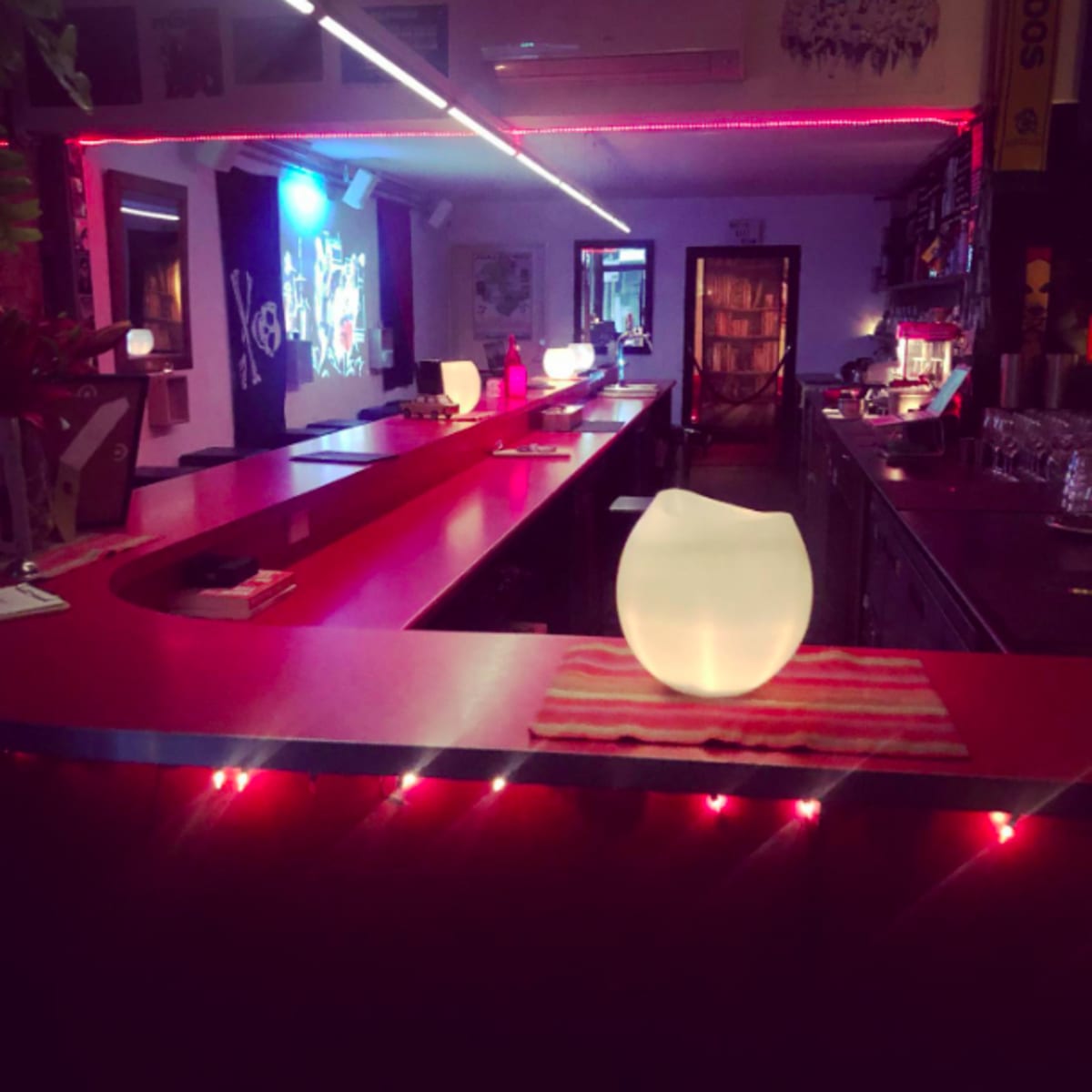 A brightly lit bar features a red counter with illuminated decor and vibrant colors reflecting off the walls.