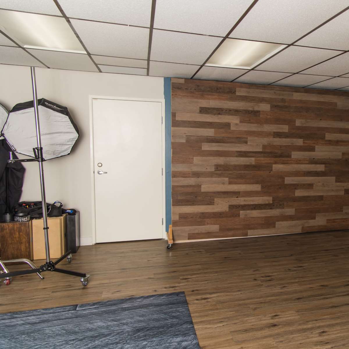 An empty room with a wood-paneled wall, a door, a mirror, and various items for photo or video production.