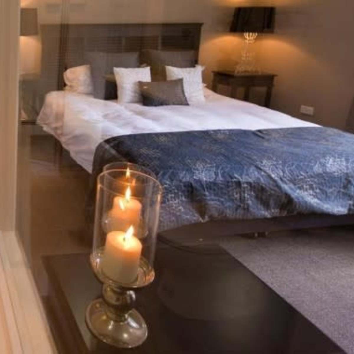 A modern bathroom with a toilet and sink adjacent to a bedroom featuring a large bed with decorative pillows.
