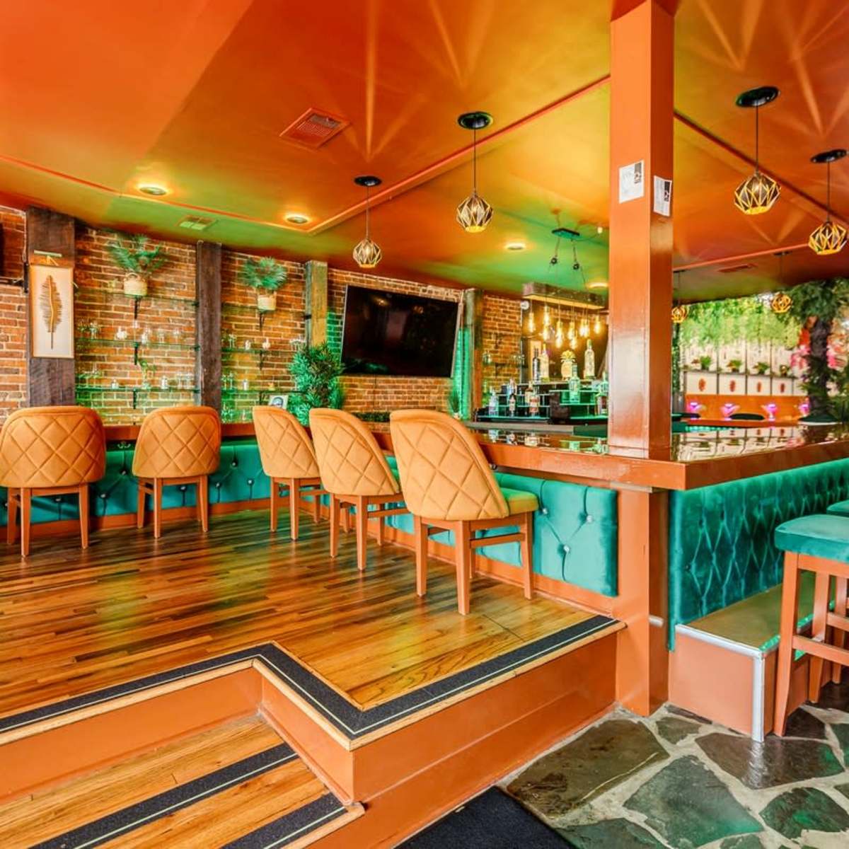 A vibrant restaurant interior featuring orange and green seating, wooden flooring, and exposed brick walls.