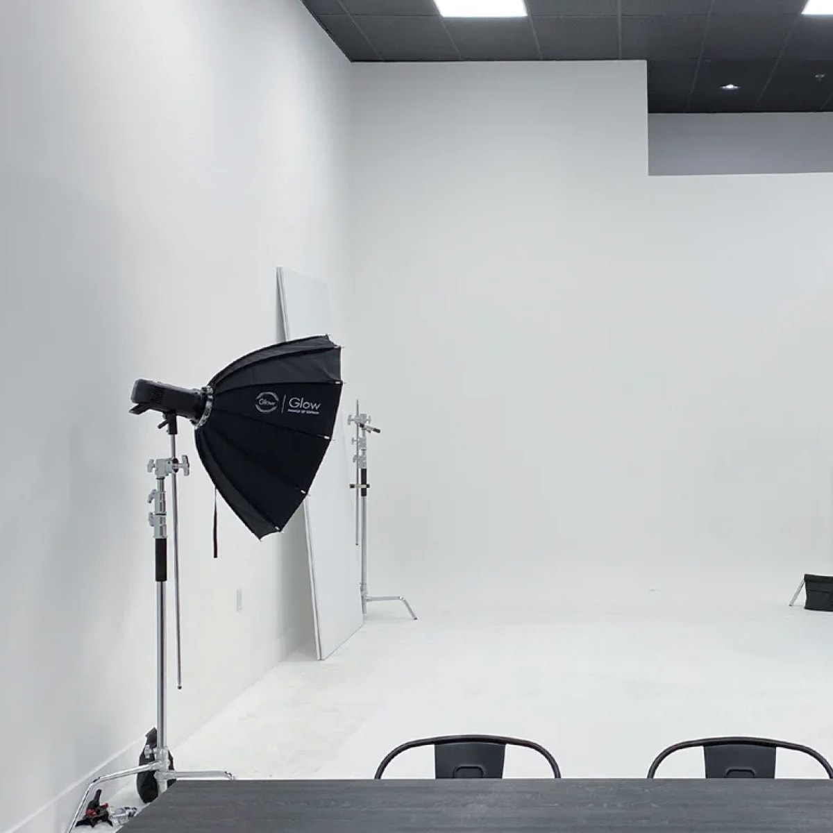 A minimalist studio space with white walls, a light gray floor, and two black softbox lights positioned on either side.