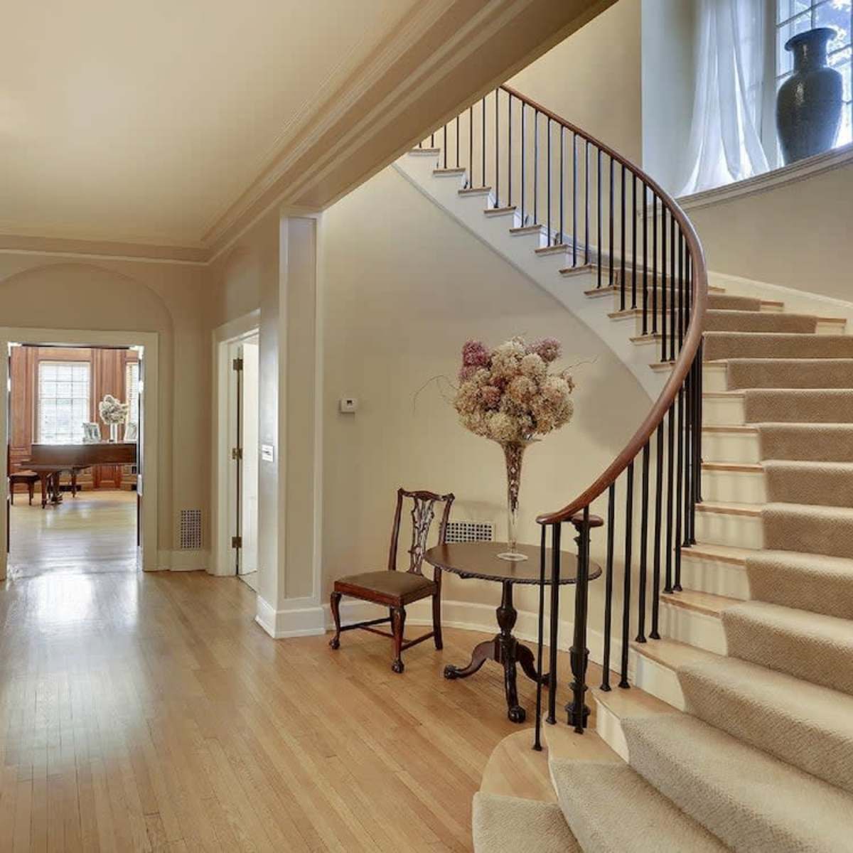A spacious hallway with a staircase on the right, leading to an upper level, and a floral arrangement on a table near the entrance.