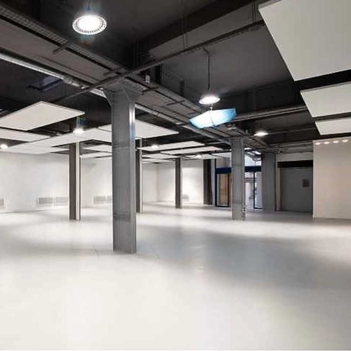 A spacious, well-lit room with a smooth white floor and exposed structural beams.