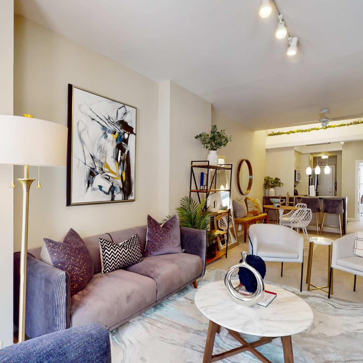 A modern living room with a purple couch, decorative artwork on the wall, and a round marble coffee table.