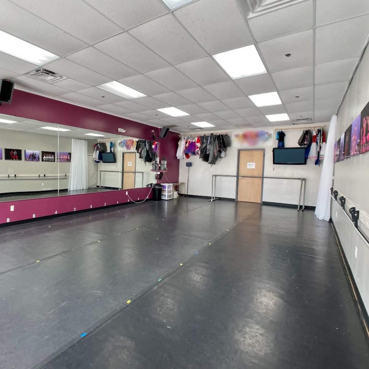 A dance studio with a mirrored wall, a dark floor, and various costumes hanging nearby.
